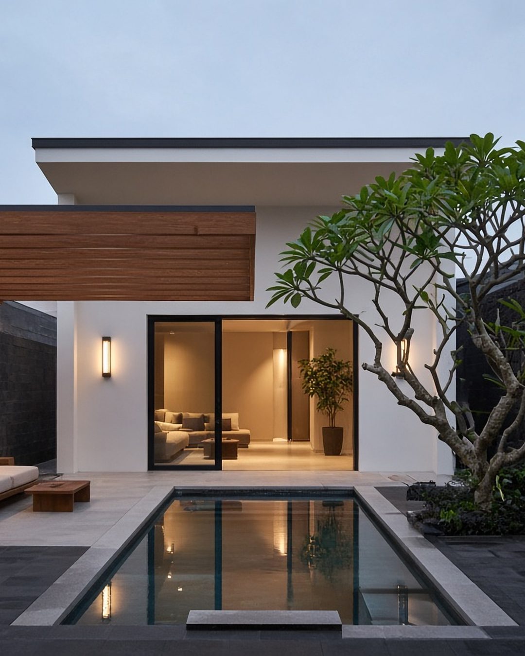 Meghvan Courtyards: a basalt and lime-plaster villa at dusk with a timber pergola and a small lap pool (artist's impression)